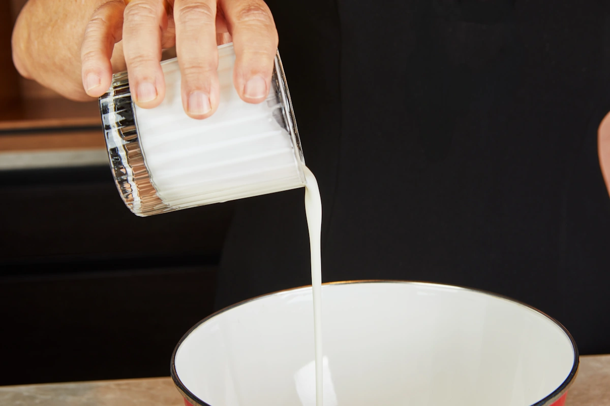 Une personne qui verse de la crème liquide entière dans un bol pour préparer du panna cotta